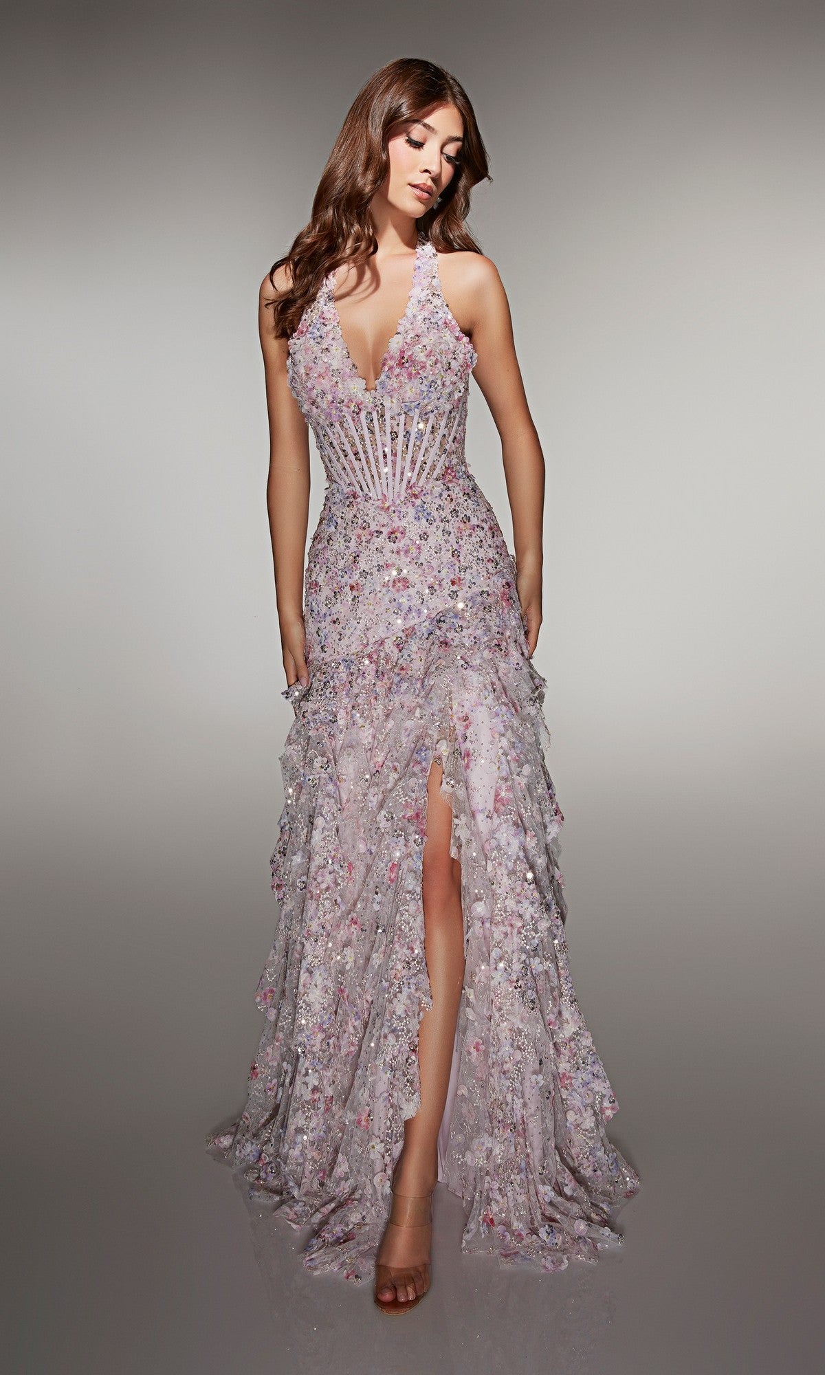 A woman models the Alyce 61999 Long Prom Dress, featuring a sleeveless floral pattern, fitted corset bodice, deep V-neckline, ruffled floor-length skirt with a front slit, standing against a plain background.